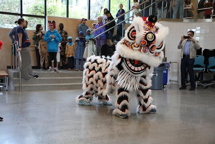 two people dressed in a white lion dancer costume at the bottom of a stairway with people watching from the stairs